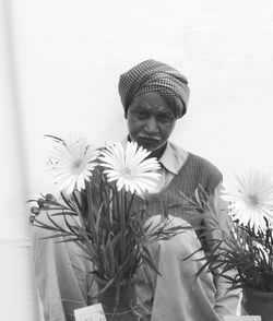 Portrait of mature vendor selling flower pots while sitting against wall