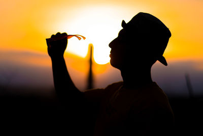 Silhouette man holding orange against sky during sunset