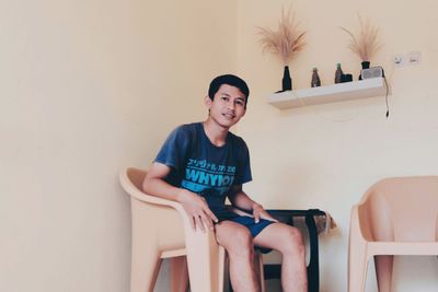 Portrait of smiling man sitting on seat against wall