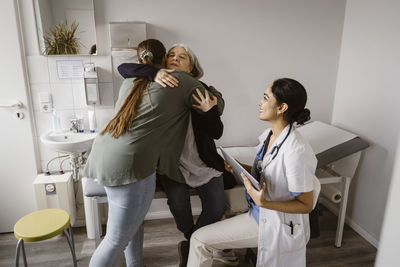 Daughter embracing mother sitting on bed by daughter in clinic