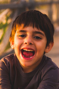 Portrait of smiling boy with mouth open sitting outdoors
