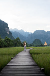 Rear view of man walking on boardwalk against sky
