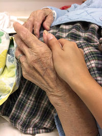 Cropped image of woman holding grandmother hands lying on bed