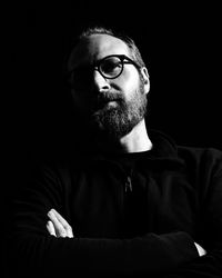 Close-up portrait of man wearing eyeglasses against black background