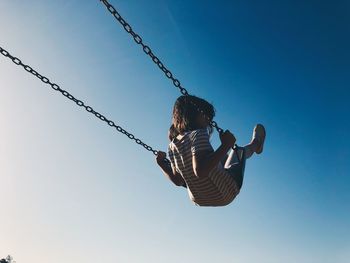 Rear view of woman on swing at playground against sky