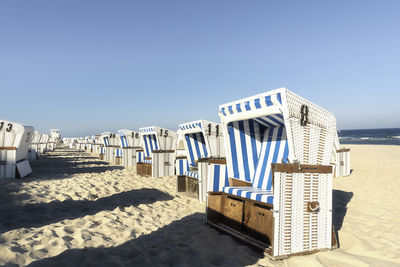 Hooded chairs on beach against clear blue sky