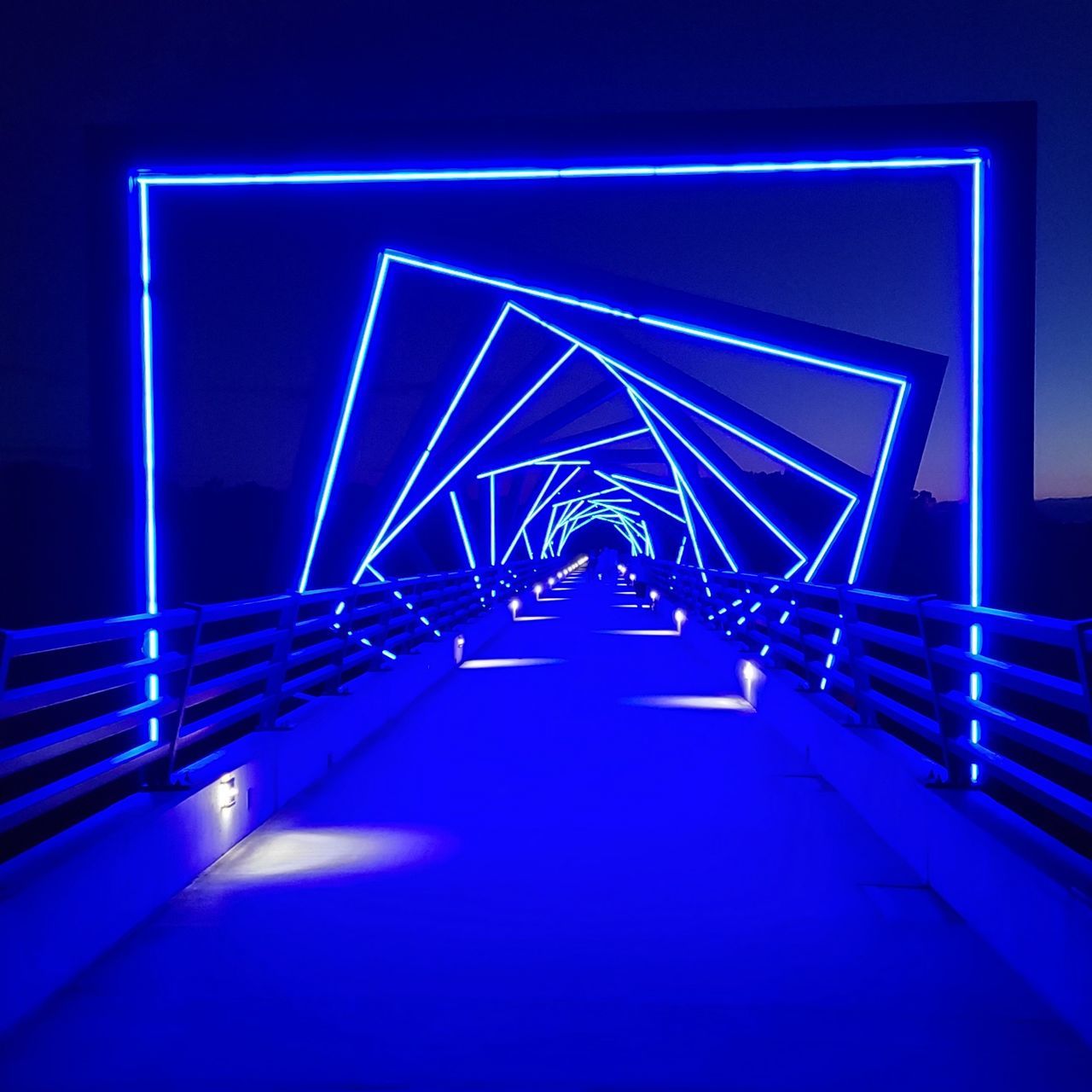 ILLUMINATED FOOTBRIDGE OVER BLUE LIGHT AT NIGHT