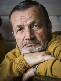 Portrait of senior man wearing sweater leaning on wooden railing while sitting at home