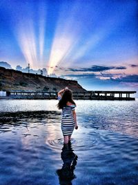 Rear view of woman standing on shore against sky