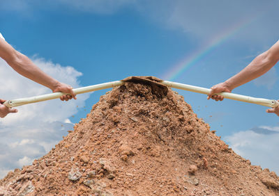 Multiple image of worker holding shovel on dirt heap against sky
