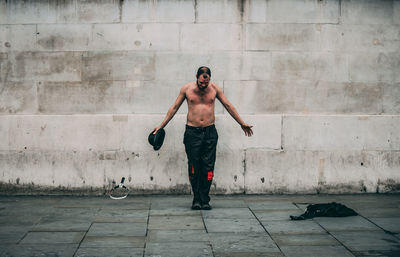 Full length of shirtless man standing against wall