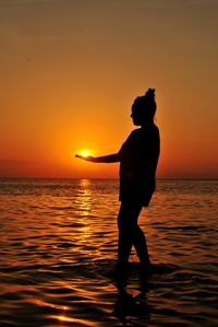 Silhouette man standing on sea against sky during sunset