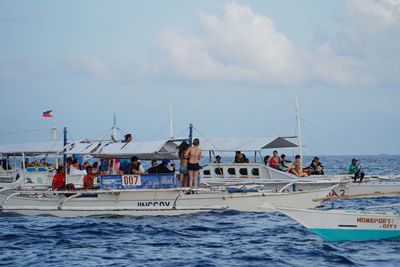 People on boats sailing in sea against sky