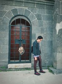 Full length of young man standing against brick wall