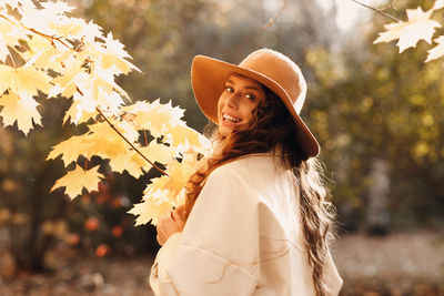 Young woman wearing hat standing against tree
