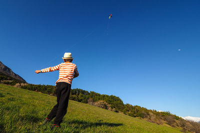 Rear view of man standing on field against clear blue sky