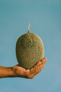 Close-up of hand holding apple against blue background