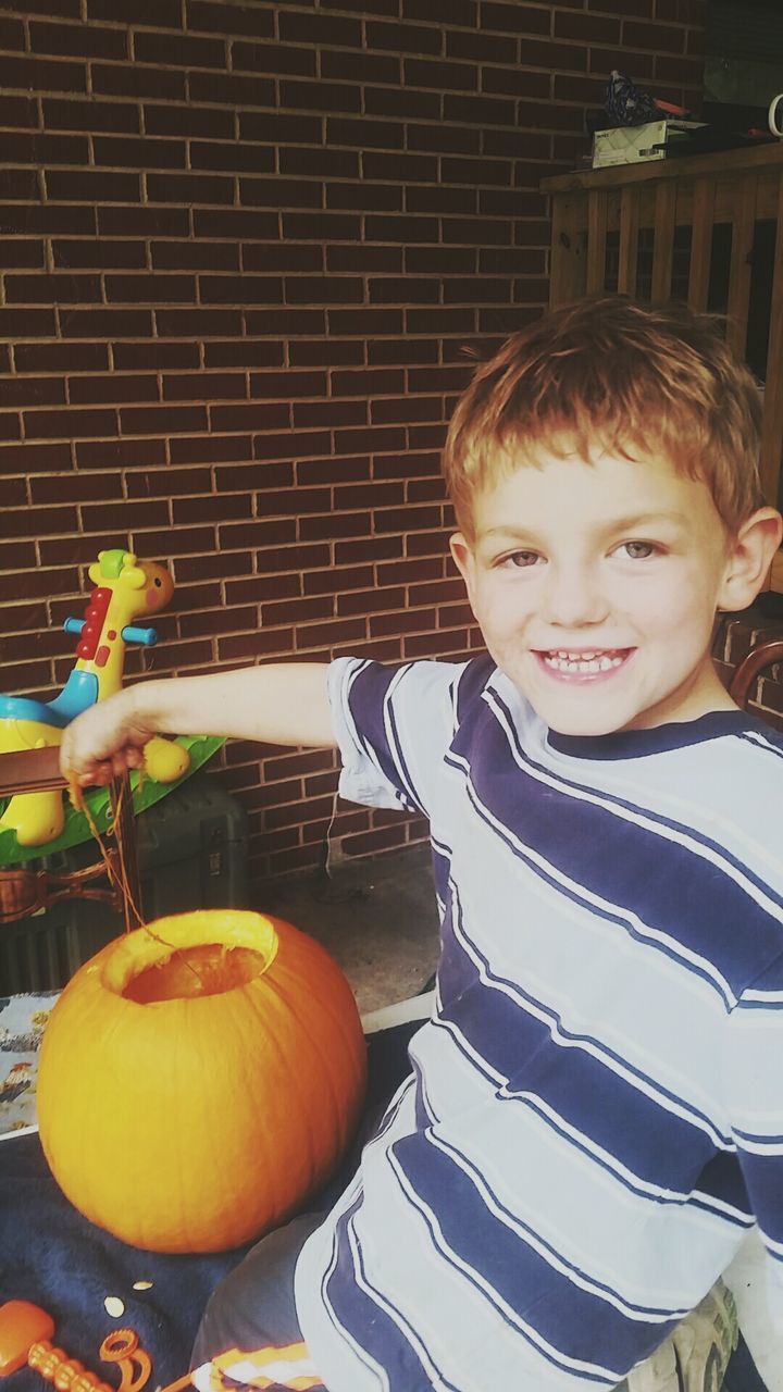 PORTRAIT OF SMILING BOY BY PUMPKIN AGAINST WALL