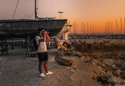 Full length of boy standing on sea shore against sky during sunset