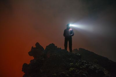 Woman with head torch standing against orange sky