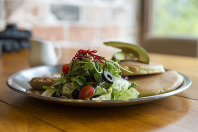 Close-up of pancakes with salad and sausage served in plate on wooden table