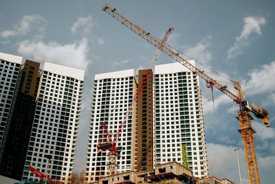 Low angle view of crane by building against sky