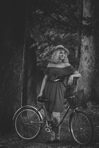 Full length of woman standing with bicycle against trees in forest