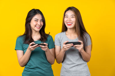 Portrait of a smiling young woman standing against yellow background