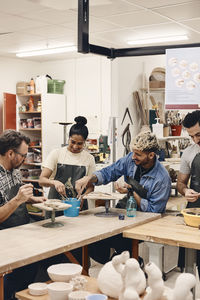 Smiling woman sharing work tools with artists sitting at table in art class