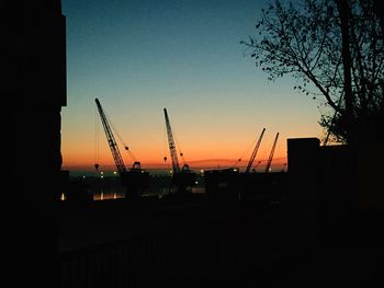 Silhouette of cranes against sky during sunset