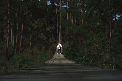 Rear view of woman walking on footpath amidst trees in forest