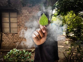 Man holding leaf while standing amidst smoke