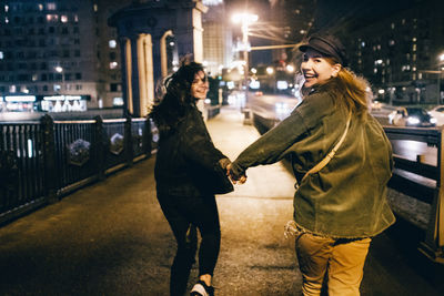 Smiling friends walking on road in city at night