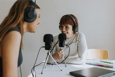 Happy teenage girls talking during podcast at desk in classroom