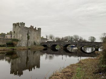 Arch bridge over river by buildings against sky