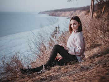 Young woman sitting on land against sky