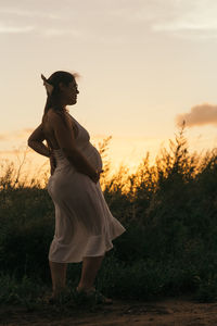 Side view of woman standing on field against sky during sunset