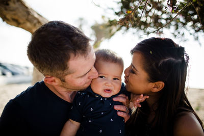 Parents kissing son while sitting under tree