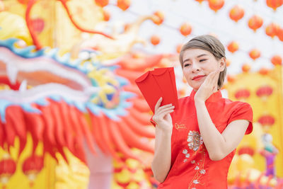 Young woman with red umbrella standing against orange wall