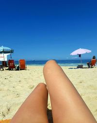 Low section of woman relaxing on beach against clear blue sky