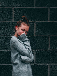 Portrait of proud girl standing against brick wall