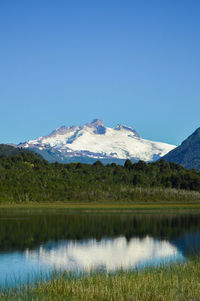 Scenic view of lake and snowcapped mountains against clear blue sky