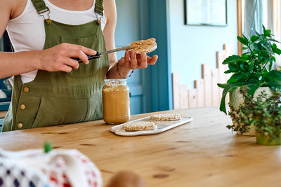 Woman making healthy breakfast or brunch, spreading peanut butter on a puffed corn cakes.