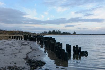 Wooden posts in sea against sky