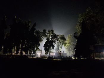 Silhouette trees by illuminated building against sky at night