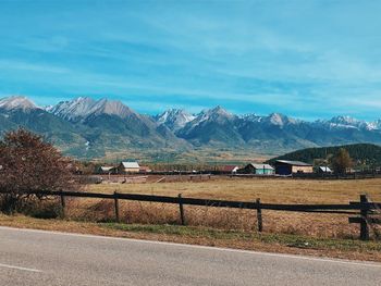 Road by buildings and mountains against sky