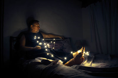 Man with illuminated lighting equipment sitting on bed