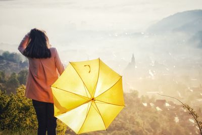 Rear view of woman with umbrella standing against land