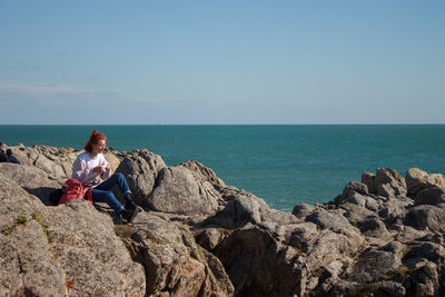 Girl sitting on rock by sea against sky