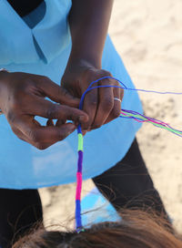 Midsection of woman braiding female friend hair with multi colored strings